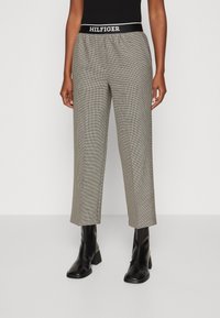Harmaat ja mustat ruudulliset housut, joissa on vyötärönauhassa "HILFIGER"-logo, rento istuvuus ja lyhennetty pituus, yhdistettynä mustiin nilkkureihin.