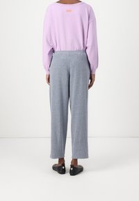 Vaaleanliila pitkähihainen paita, jossa on rento istuvuus ja pyöreä kaula-aukko; yhdistetty harmaisiin, pehmeistä materiaaleista valmistettuihin leveälahkeisiin housuihin. Mustat liukuvaat sukat näkyvät.