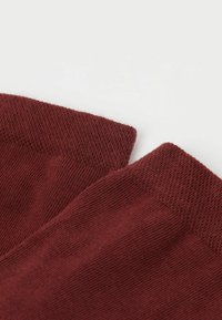 Burgundské pletené ponožky s jemnou texturou. Detailní pohled ukazující měkké žebrované manžety a hladké tělo. Bez vzorů nebo viditelného hardwaru.