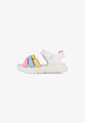 Sandalia blanca para niños con tiras anudadas en rosa, azul y amarillo y una tira de velcro en el tobillo sobre una suela blanca gruesa.