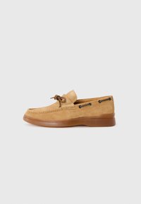 Mocassin en suède de style léger en brun clair avec une semelle en caoutchouc. Présente un laçage et des œillets en métal sur les côtés. Fini lisse, design minimal.