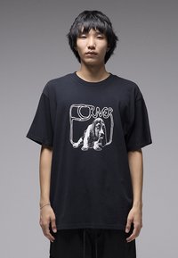 Μαύρο βαμβακερό μπλουζάκι με λευκό γραφικό σχέδιο ενός σκύλου και τη λέξη «CORNER» σε καμπύλη γραμματοσειρά. Άνετη εφαρμογή με κοντά μανίκια.