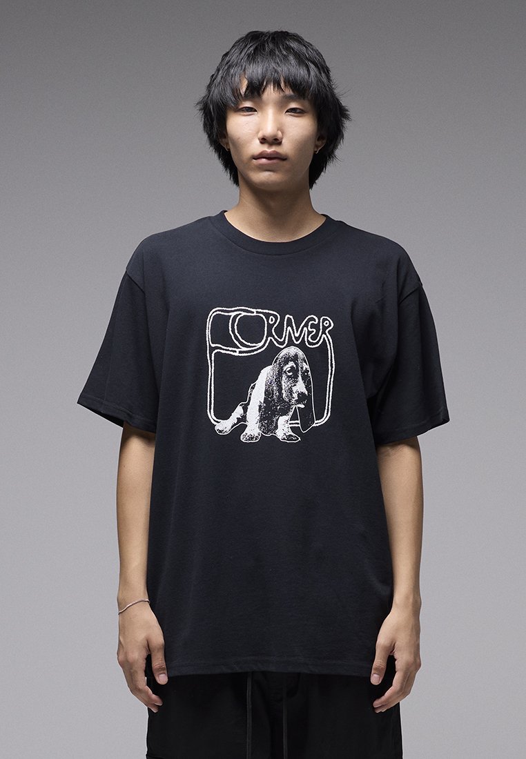 Μαύρο βαμβακερό μπλουζάκι με λευκό γραφικό σχέδιο ενός σκύλου και τη λέξη «CORNER» σε καμπύλη γραμματοσειρά. Άνετη εφαρμογή με κοντά μανίκια.