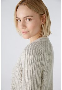 Helles beige gestricktes Sweatshirt mit strukturierter Ripp-Optik, Rundhalsausschnitt und leicht überschnittenen Schultern. Einfaches, lässiges Design.