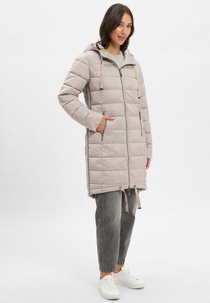 Padded long coat in light beige, featuring a hood, zip closure, and drawstring at the hem. Styled with gray jeans and white sneakers.