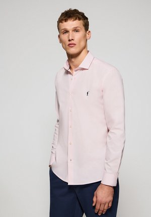 Camisa de botón de color rosa claro fabricada con tela suave, con un corte ajustado, cuello puntiagudo y un pequeño logo en navy en el pecho.