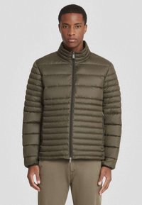 Olijfgroene pufferjas met een hoge kraag, horizontaal baffle-ontwerp, ritssluiting aan de voorkant en elastische manchetten. Glad, glanzend stoffen textuur.
