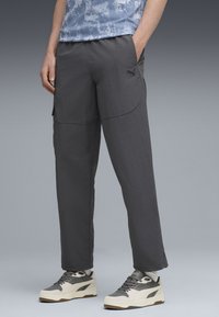 Graue Cargo-Hosen aus leichtem Material, mit Seitentaschen und lockerer Passform. Kombiniert mit grauen und cremefarbenen Sneakern.