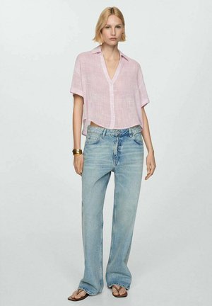 Chemise en lin rose à boutons et manches courtes associée à un jean bleu clair à jambes larges. Portée avec des sandales plates et un bracelet en or.
