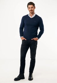 Mörkblå v-ringad tröja i mjukt material, bärs med en vit skjorta med krage under, ihop med svarta jeans och svarta snörstövlar.