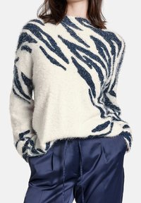 Pull blanc duveteux à motif rayures de tigre bleu marine, col rond, coupe décontractée, associé à un pantalon en satin bleu marine, poches latérales visibles.