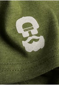 Groene katoenstof met een witte afbeelding van een schedel die een hoed draagt, met een snorontwerp. Zachte textuur met minimale stikdetails.