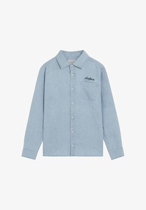 Camisa de mezclilla azul claro de manga larga con botones y un bolsillo en el pecho, con "Scalpers" bordado encima del bolsillo.