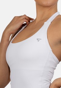 Bela atletska majica brez rokavov z tankimi naramnicami, z izrezom v obliki krogle in teksturiranimi detajli. Siva logotip na levi strani. Gladka tekstura blaga.