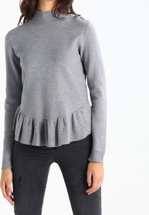 Pull en maille gris avec un col montant et un ourlet à volants. Manches longues et texture lisse, associé à un jean sombre.