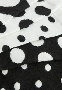 Czarno-białe skarpetki z wzorem w kropki, z kropkami o różnych rozmiarach na miękkim, teksturowanym materiale. Trzy pary ułożone jedna na drugiej.