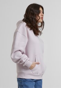 Sweatshirt à capuche rose clair avec une poche sur le devant, des poignets côtelés et une coupe ample. Tissu doux et texturé avec une silhouette décontractée.