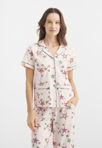 Conjunto de pijama de manga corta en algodón color rosa claro, con patrones de estrellas de colores variados, con un acabado en azul a contraste y bolsillos.