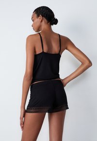 Débardeur en coton noir avec des fines bretelles assorti à un short noir avec une garniture en dentelle au bas, texture lisse et coupe décontractée.