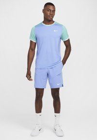 Camiseta deportiva azul claro con acentos en verde menta, combinada con pantalones cortos a juego. Presenta el logo de Nike en el pecho y en los pantalones cortos. Zapatillas y calcetines blancos.