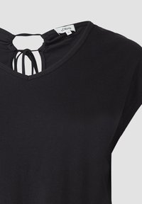 Zwarte top met korte mouwen, voorzien van een V-hals en een striksluiting aan de achterkant. Gemaakt van zachte stof met een gladde tekstuur. Maatlabel zichtbaar.