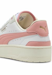 Fehér bőr sneaker rózsaszín kiegészítőkkel, texturált sarokrésszel, arany márkajelzéssel és vastag, krémszínű gumi talppal. Perforált részletek találhatók rajta.