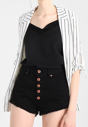 Kvinde iført en sort V-hals top, højttaljede sorte shorts med seks synlige knapper og en hvid åben blazer med pinstriber.
