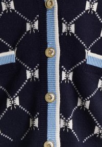 Cardigan en maille bleu marine avec bordure rayée blanche et bleu clair, boutons dorés et motif papillon blanc sur le tissu.