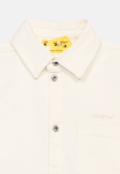 Chemise à col blanc avec des boutons-pression argentés, une poche poitrine, et une étiquette jaune portant l'inscription « Off-White » conçue à Milan, en Italie.