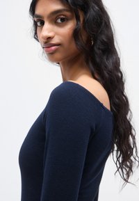 Μπλούζα σε ναυ τικό μπλε χρώμα με μακριά μανίκια και λαιμόκοψη εκτός ώμου. Μαλακό, υφασμάτινο με υφή και εφαρμοστή σιλουέτα.