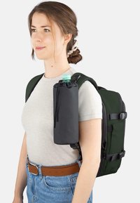 Schwarzer Rucksack mit verstellbaren Trägern und Flaschenhalter. Das Material ist strapazierfähiger Stoff, die Farbe dunkelgrün. Freizeitoutfit mit hellgrauem Hemd.
