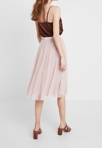 Ruskea satiinitoppi, jossa on säädettävät spaghetti-hihnat, yhdistetty vaaleanpunaiseen pleated-tyllihameeseen ja ruskeisiin paksupohjaisiin sandaaleihin.