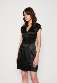 Robe en satin noir avec un corsage ajusté, des manches courtes et un décolleté en V. Possède une fermeture à boutons sur le devant et une jupe évasée. Texture lisse.