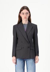 Blazer gris à rayures fines croisé avec larges revers, deux poches avant et boutons noirs. Porté sur un haut coloré et associé à un jean bleu.
