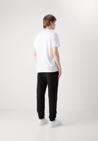 Λευκό βαμβακερό μπλουζάκι με κοντά μανίκια, συνδυασμένο με μαύρες φόρμες με ελαστικές μανσέτες, φορεμένο με λευκά αθλητικά παπούτσια.