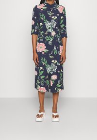 Abito floreale con sfondo blu navy e fiori rosa e verdi, collo a punta e maniche a tre quarti. Completo di cintura da annodare.