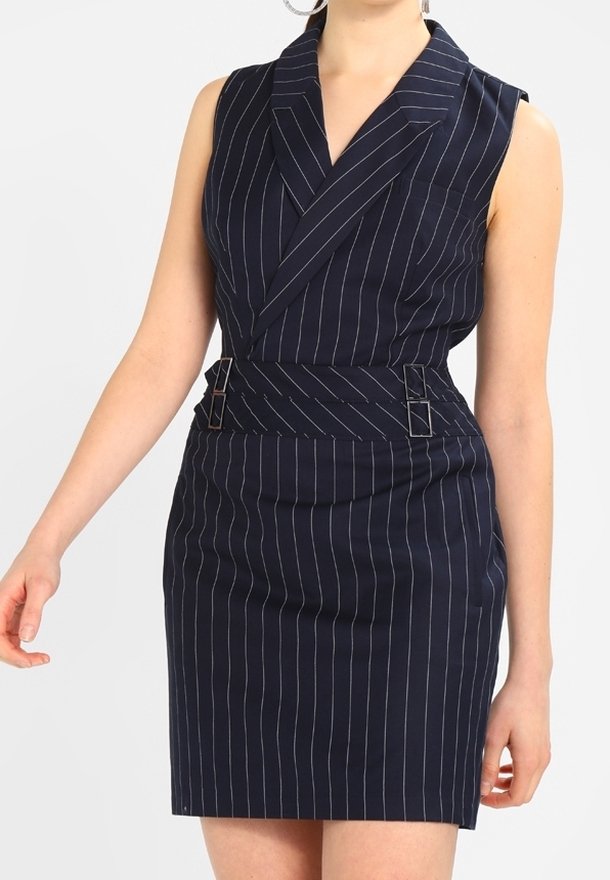 Femme portant une robe bleu marine sans manches à rayures fines avec une large ceinture et un col à revers.