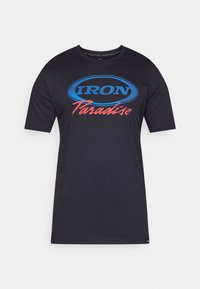 Sort kortærmet T-shirt lavet af bomuld. Har "IRON" i blå og "Paradise" i rød grafisk tryk foran inden for en oval kontur.