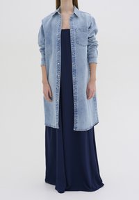 Vaaleansininen farkkutakki pitkille hihoille ja rintataskulle, kerrostettuna tummansiniselle maksimekkoon, esittäen rentoa istuvuutta.