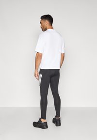 Vit t-shirt med korta ärmar tillsammans med svarta figurnära leggings med tre vita ränder på sidan. Svarta sportskor fulländar looken.