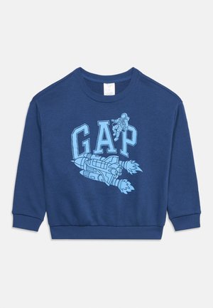 Tumesinine dressipluus tekstiga "GAP", millel on sinine rakett ja astronaud, kes hõljub tähtede kohal.