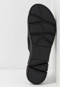 Semelle de chaussure noire avec un motif texturé, présentant des rainures angulaires et un bord lisse. Fabriquée en caoutchouc, elle offre durabilité et adhérence.