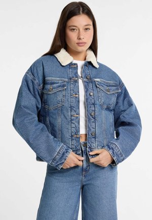 Giacca di jeans in azzurro chiaro con un morbido colletto in pelliccia sintetica bianca, dotata di chiusura a bottoni e due tasche sul petto, taglia oversize e consistenza spessa.