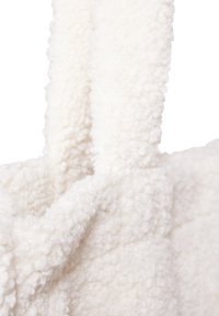 Witte, fluffy stoffen tas met een gestructureerd, zacht oppervlak. Voorzien van stevige, pluizige handvatten voor eenvoudig dragen.