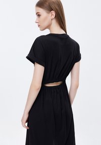 Vestido negro con mangas cortas enrolladas, cintura elástica y un detalle cortado en la espalda. Tejido suave con un corte relajado.