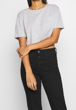 Woman wearing a light gray short-sleeve crop top and high-waisted black jeans with a button fly, standing against a plain background.