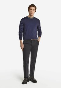 Marinblå tröja, rund halsringning, slim fit, tillsammans med mörka byxor, brunt bälte och mörka skor. Slät textur, minimal detaljer och klassisk design.