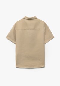 Camicia beige a maniche corte realizzata in tessuto morbido, con colletto e design minimalista, caratterizzata da uno schienale pulito e dettagli di cucitura discreti.
