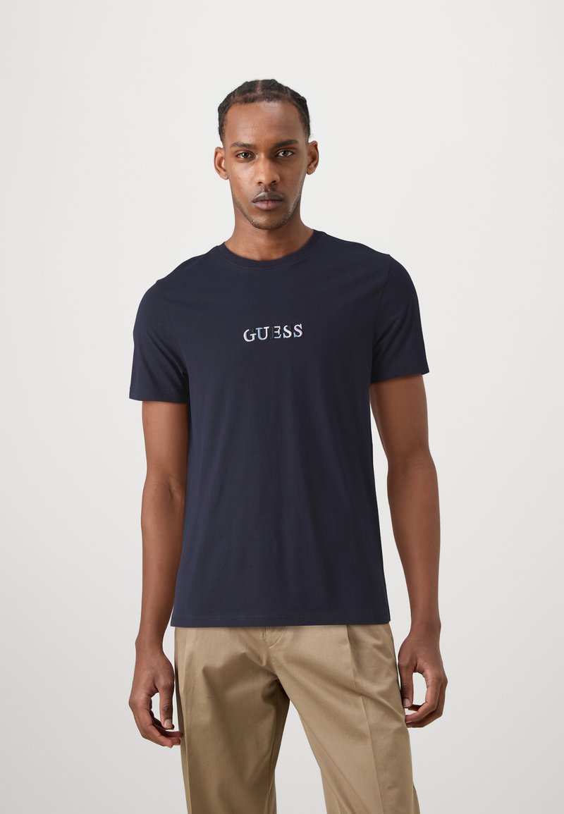 Camiseta de manga corta color azul marino hecha de algodón, con el logo bordado "GUESS" en blanco y azul claro en el pecho.