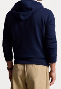 Mörkblå huvtröja med ribbade muddar, mjuk textur och kenguruficka, kombinerad med beige byxor med en detalj på bakfickan.